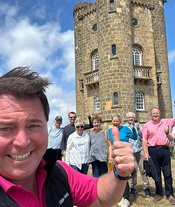 Ben and tour guests saying cheese from infront of the 18th century Broadway Tower