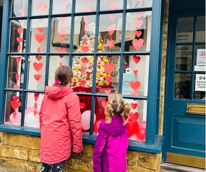 Two children looking through a shop window displaying hearts