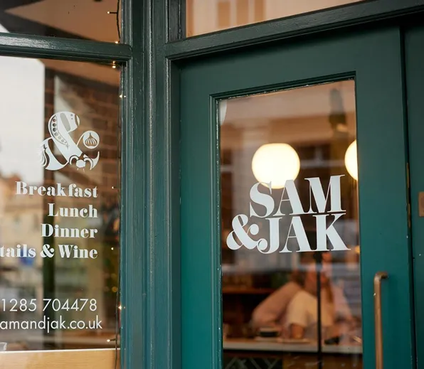 Green door and window of Sam & Jak restaurant listing meals: breakfast, lunch, dinner, cocktails, and wine.