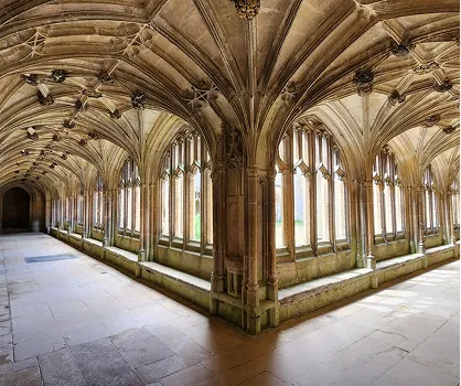 Stone corridor in a historic building with vaulted ceilings and tall arched windows on both sides.