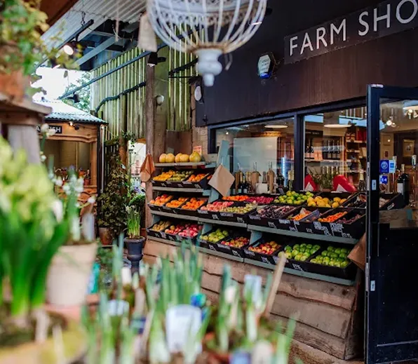 Outdoor farm shop display with assorted fresh fruits and vegetables on shelves under a sign reading Farm Shop.