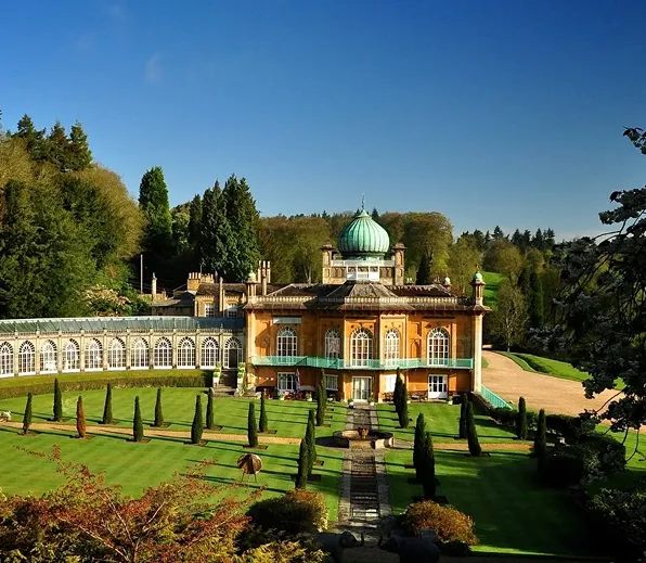 Historic mansion with a green dome surrounded by manicured gardens and tall trees under a clear blue sky.