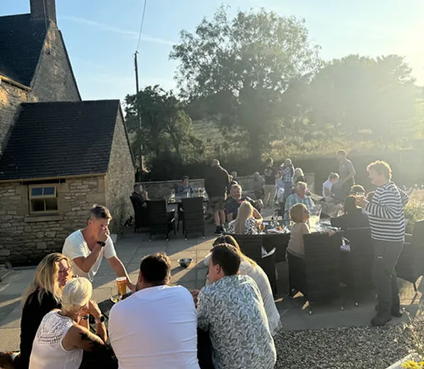People socializing outdoors on a patio near stone buildings at sunset.
