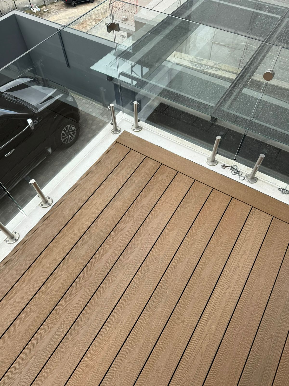 Balcón con piso de tablas de madera sintética y barandilla de vidrio con soportes metálicos.