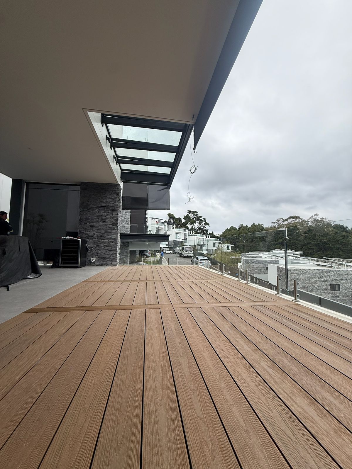 Terraza amplia con piso de madera fina y barandales de vidrio en un día nublado.