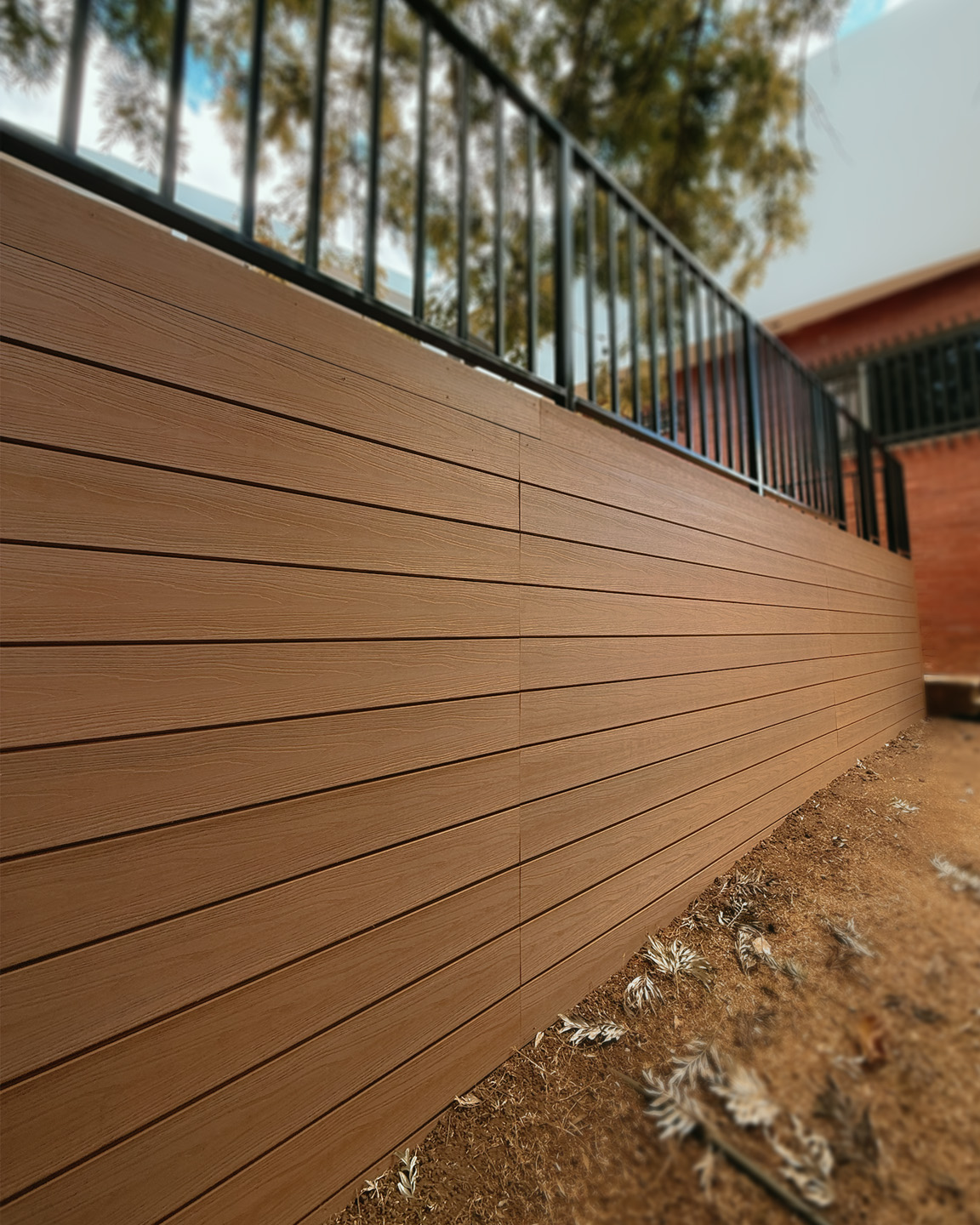 Muro exterior revestido con paneles de madera marrón bajo una baranda negra de metal.