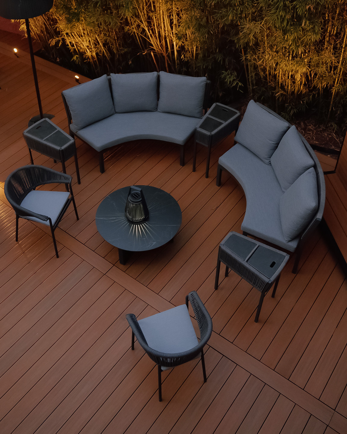 Área de terraza con muebles de exterior gris, dos sofás curvos, dos sillones, mesas y una lámpara.