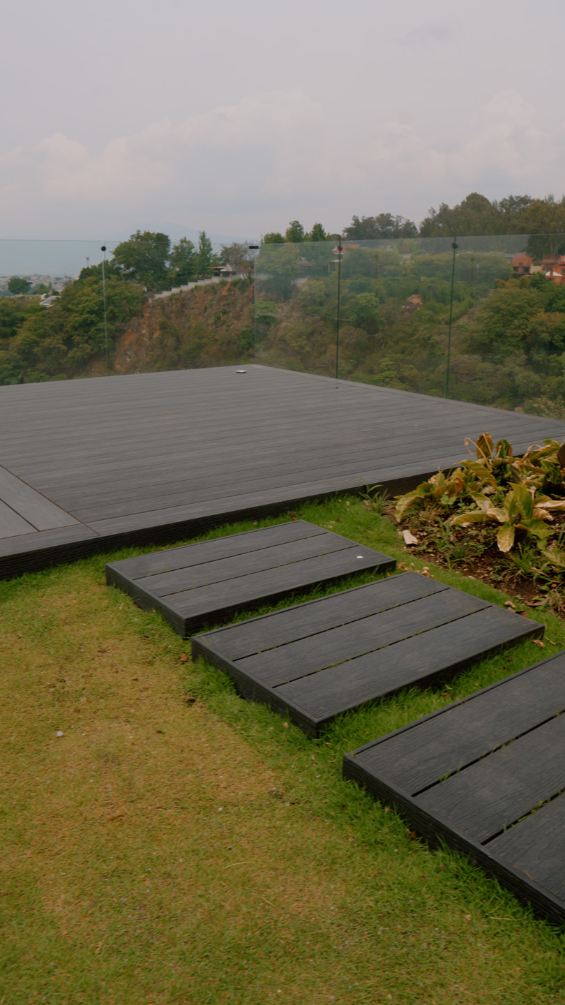 Plataforma de madera con escalones y barandilla de vidrio con vista a colinas arboladas.