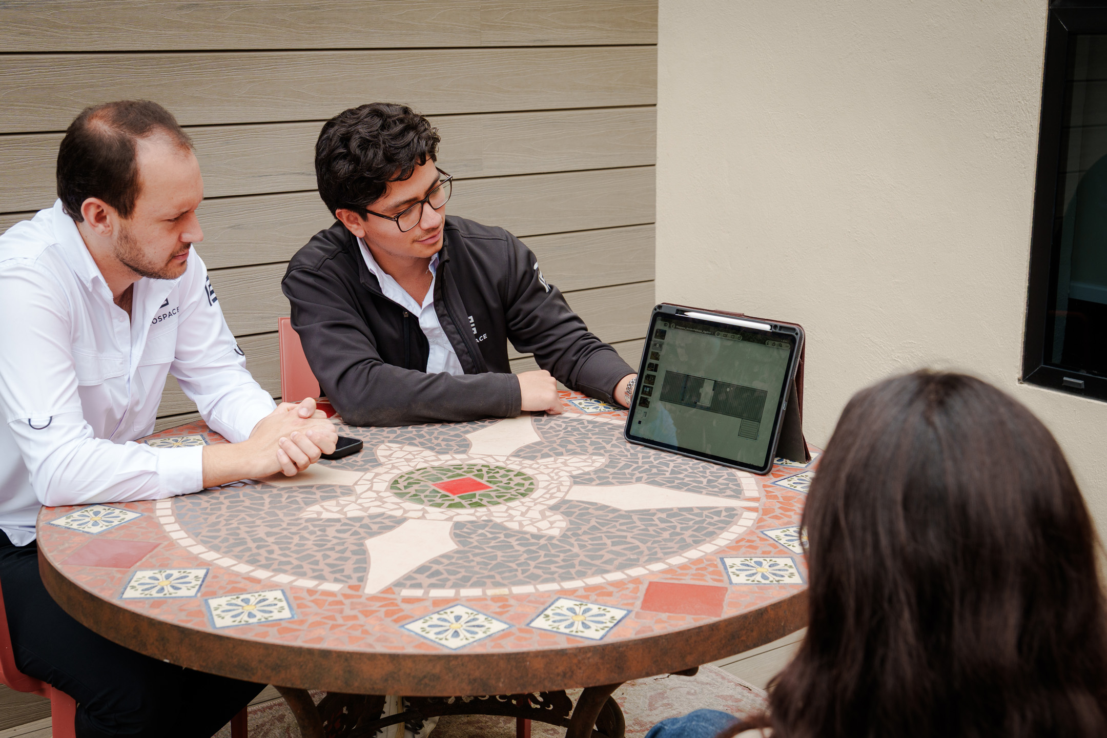 Tres personas sentadas en mesa decorativa mirando un plano arquitectónico en una tablet.