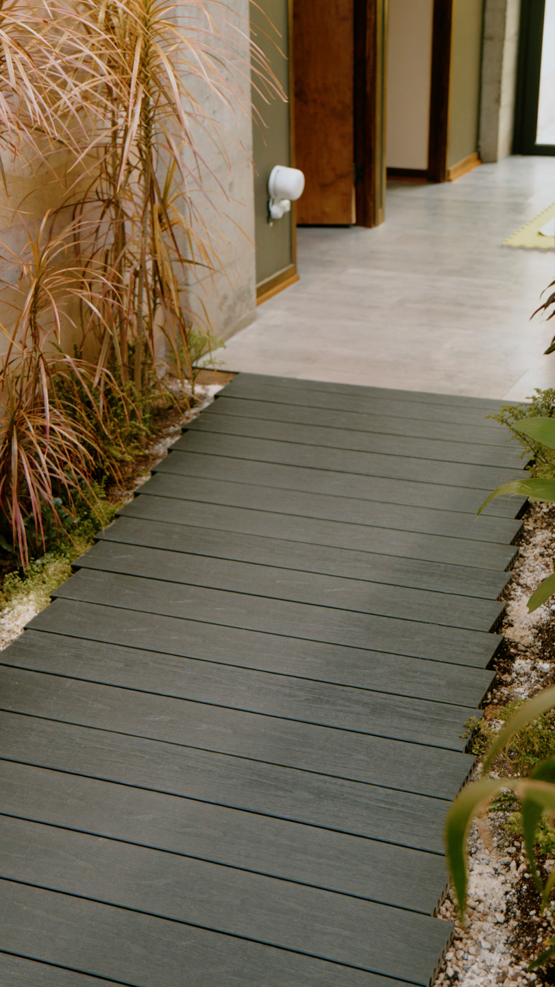 Pasillo con piso de madera oscura y plantas secas al lado izquierdo.