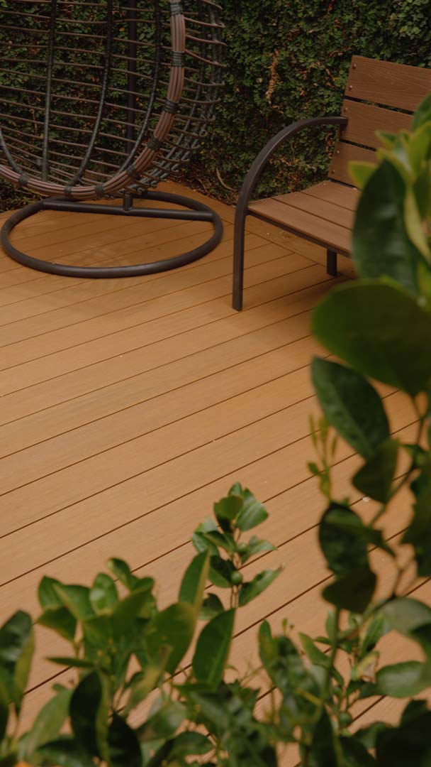 Sillón colgante y banco de madera en terraza con plantas verdes.