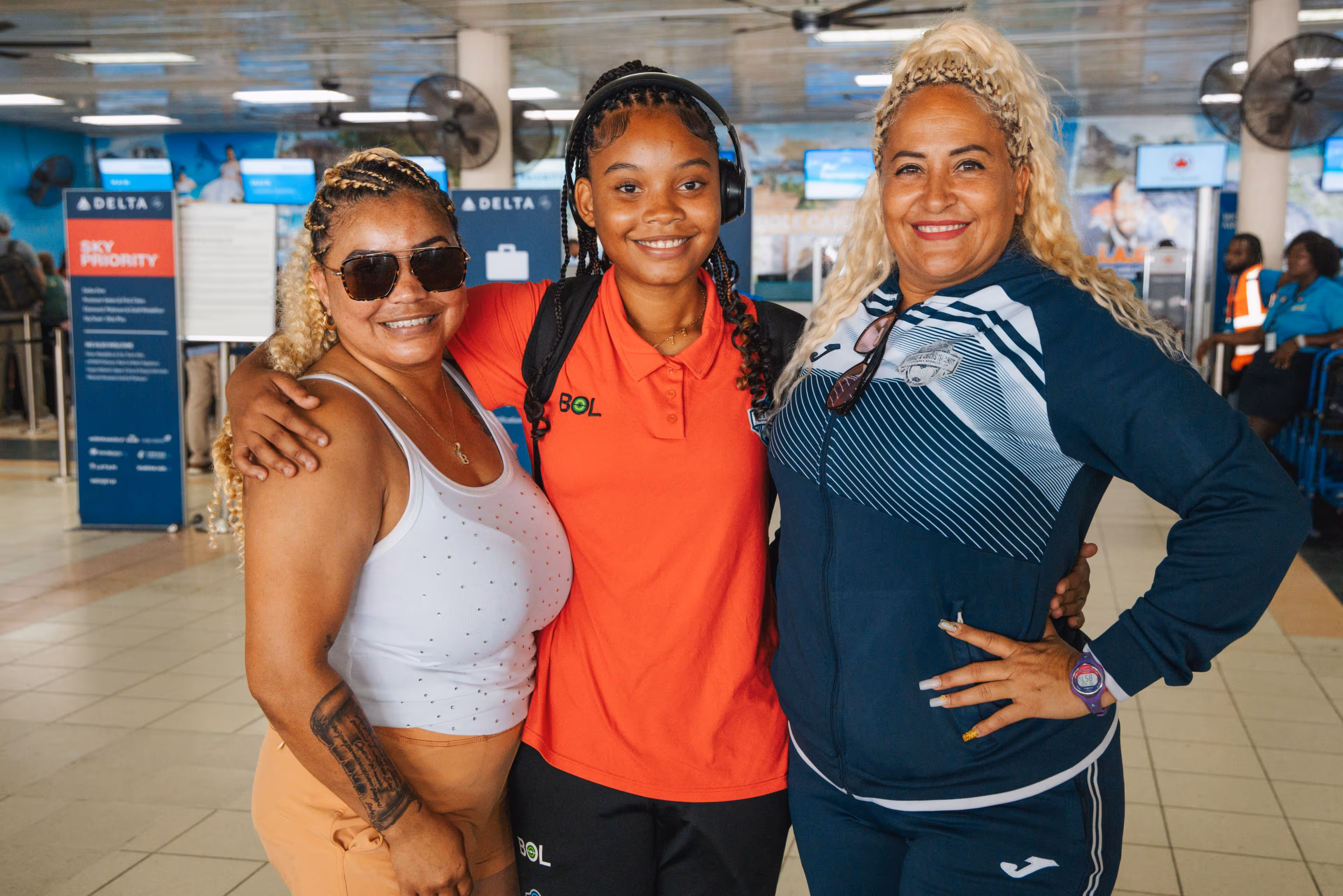 Three smiling people standing close together at an airport Delta check-in area.