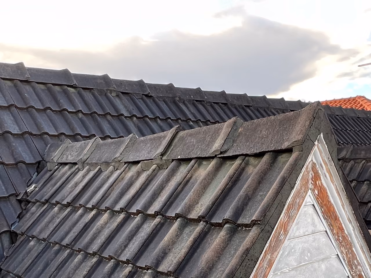 Aged concrete roof tiles with heavy cracks and missing pointing on the ridge tiles
