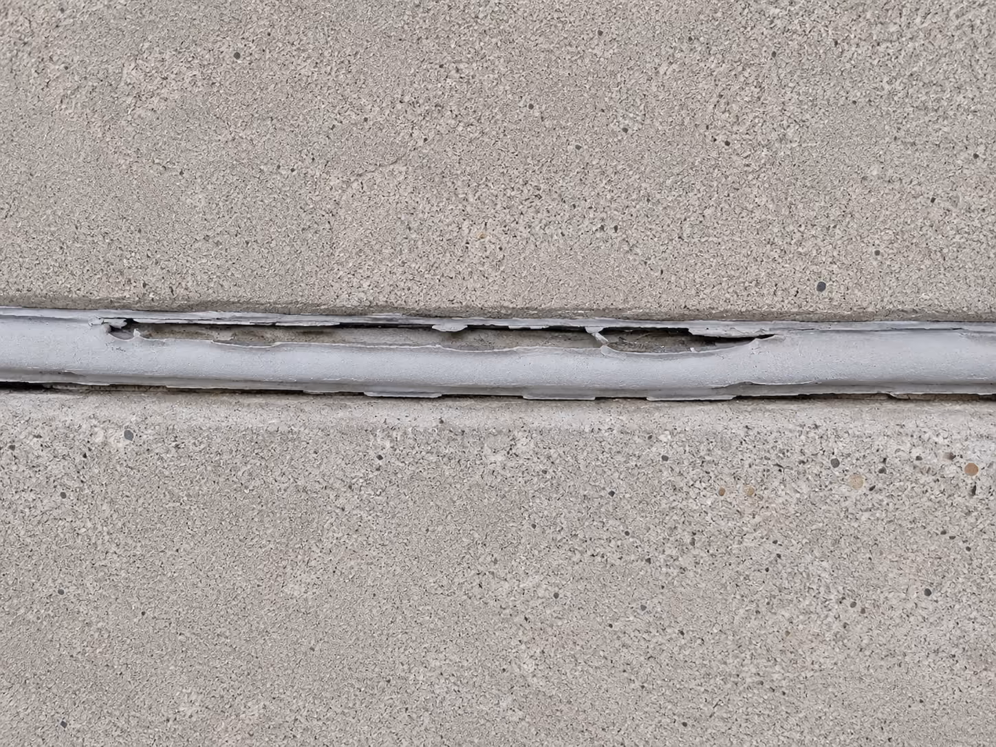 Corroding steel reinforcement bar exposed along the edge of a concrete balcony slab