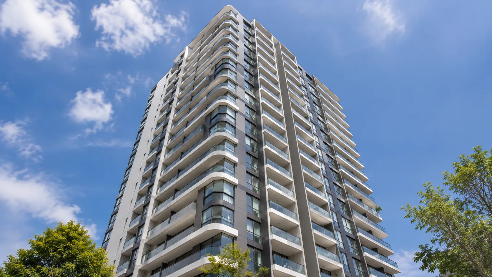 Curved-balcony residential high-rise tower viewed from ground against blue sky