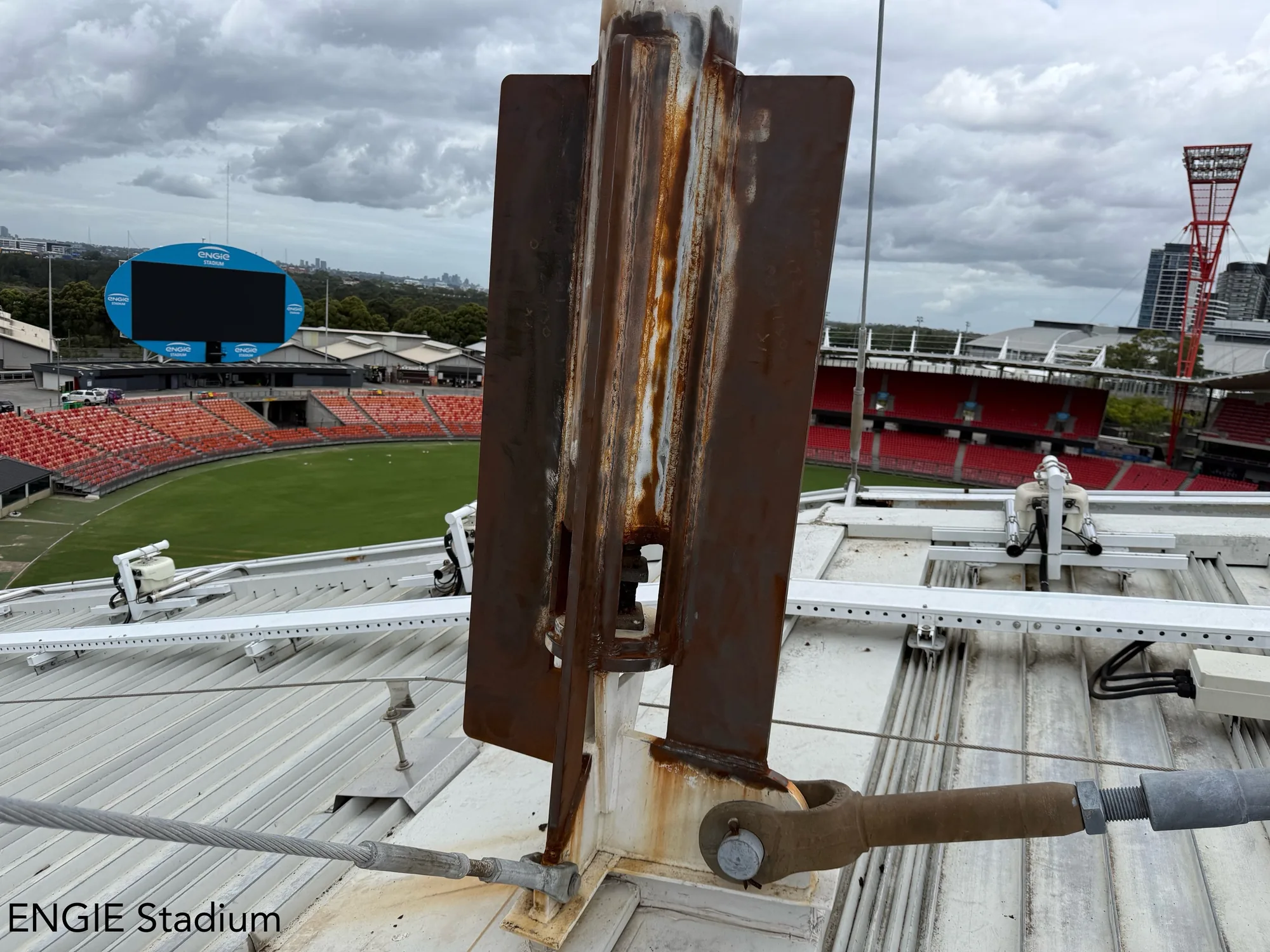 Corroded stadium roof steel mast base with heavy rust before rope-access remedial coating
