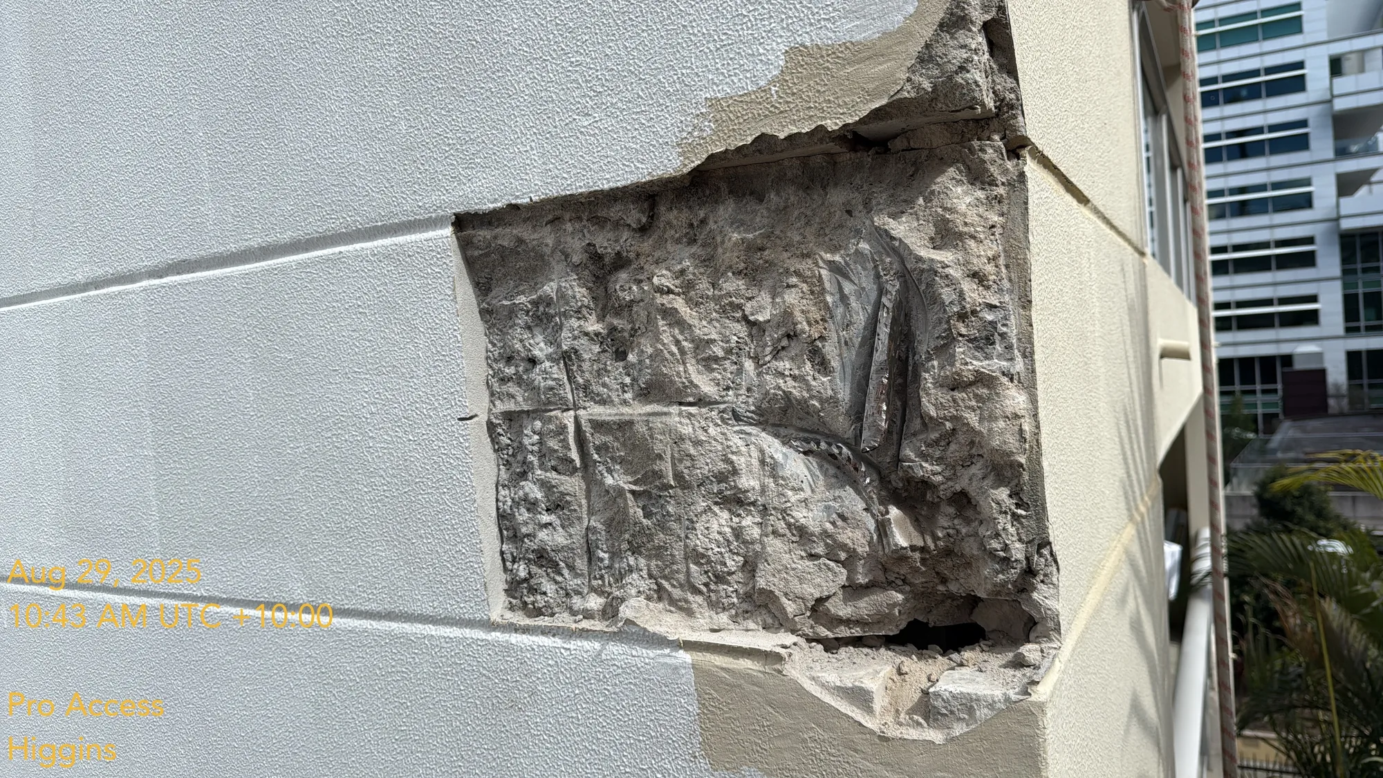Large concrete spall on rendered facade exposing corroded steel reinforcement before repair