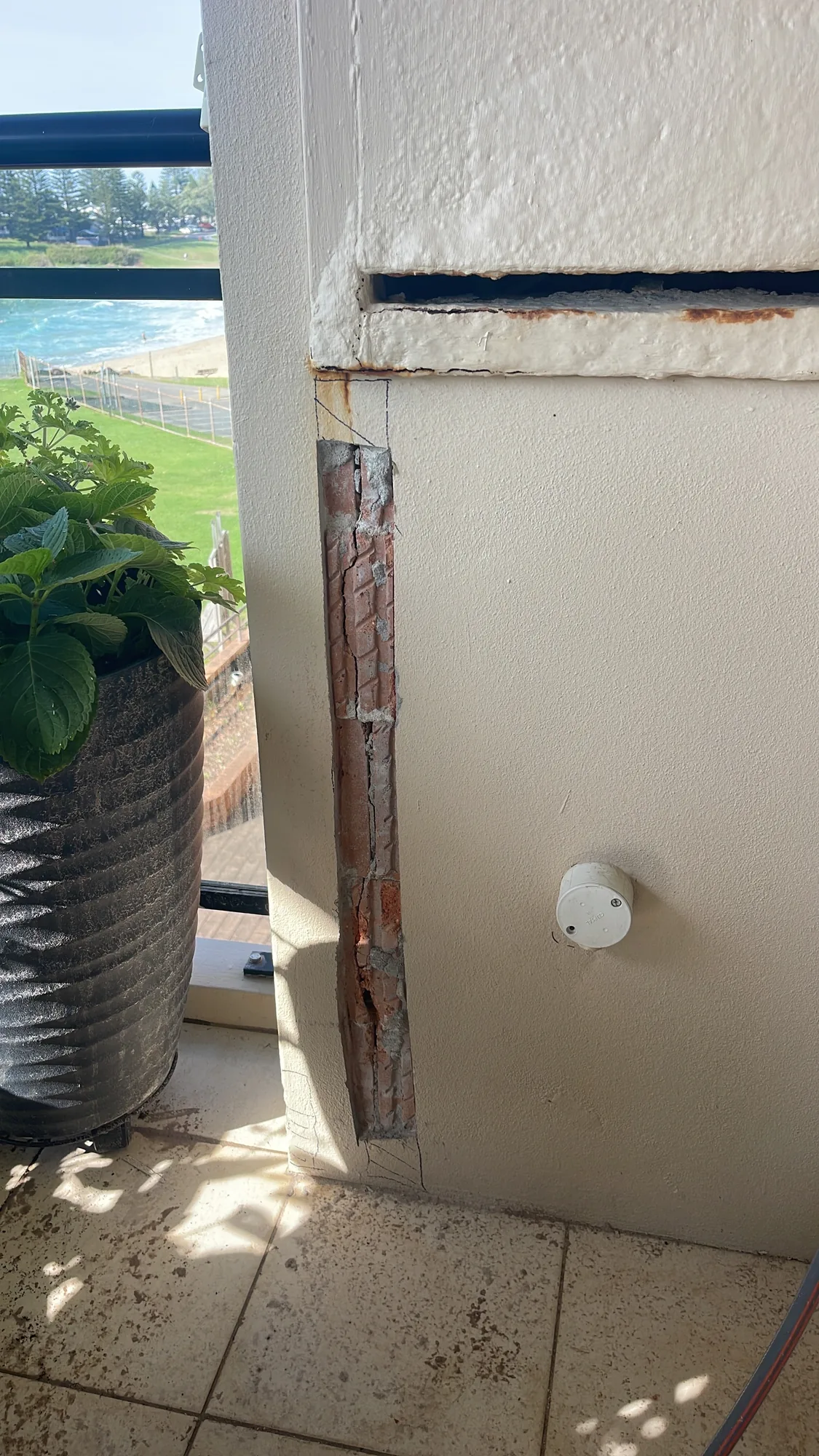 Cracked brickwork at a coastal balcony window reveal from water ingress before repair