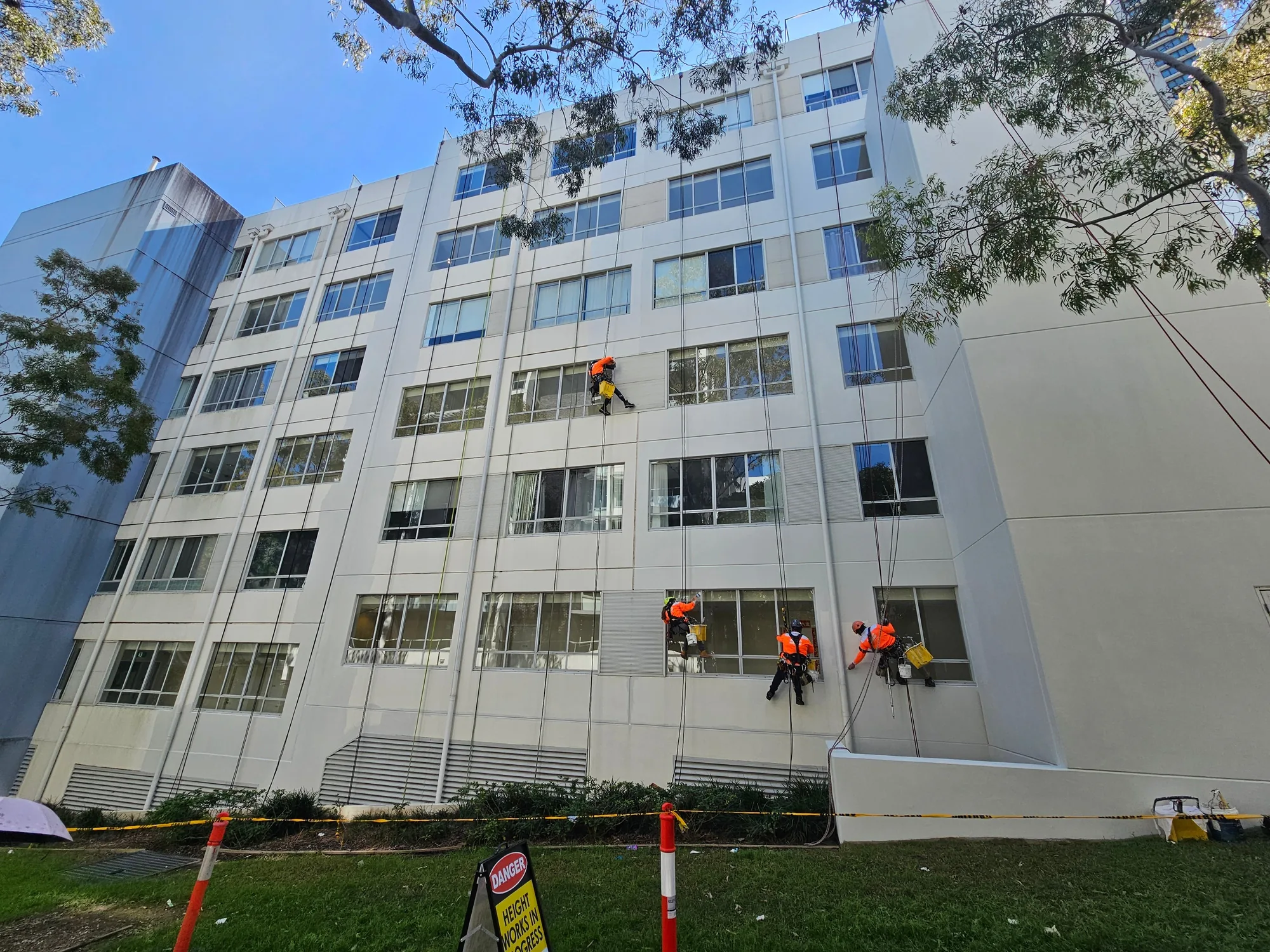 Four rope-access technicians abseiling a multi-storey Sydney facade during exterior painting