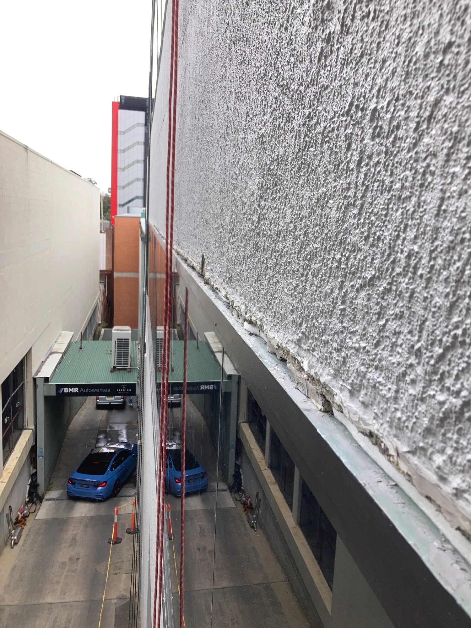 Rope lines down a rendered high-rise facade before rope-access sealant works are completed