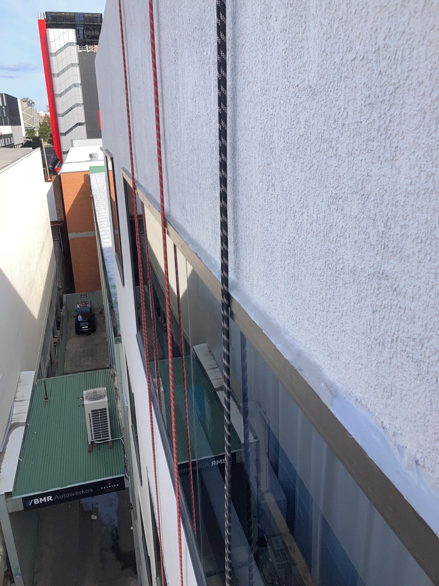 Rope lines down a rendered high-rise facade after rope-access sealant works are completed