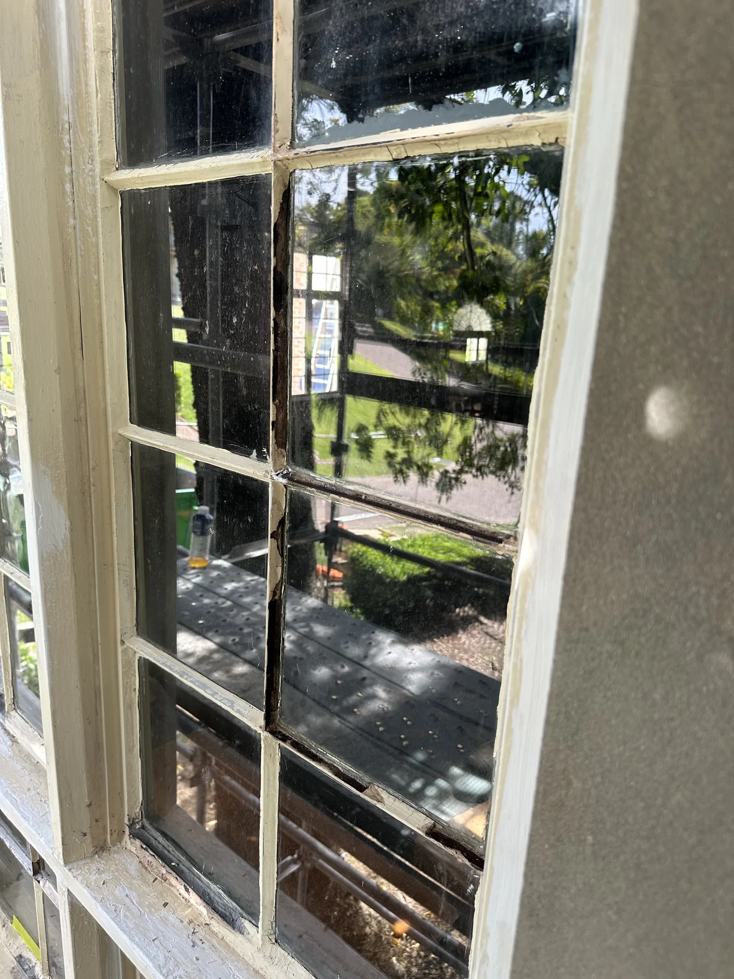 Cracked glazing on a heritage timber-framed multi-pane window before glazing repair and painting