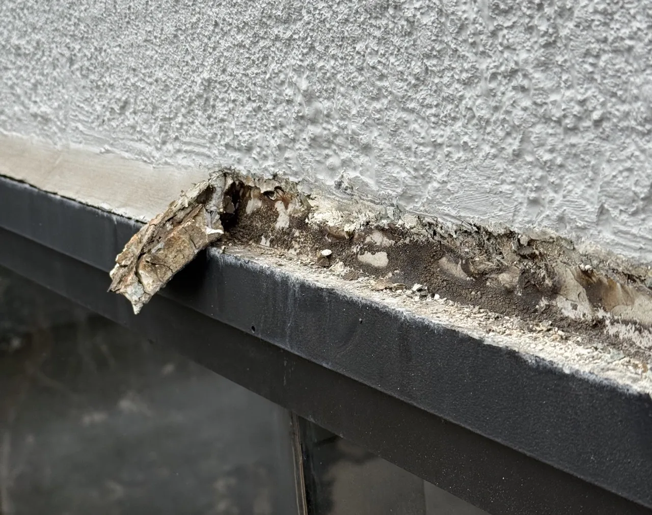 Failed sealant above a window frame, showing mould behind it.