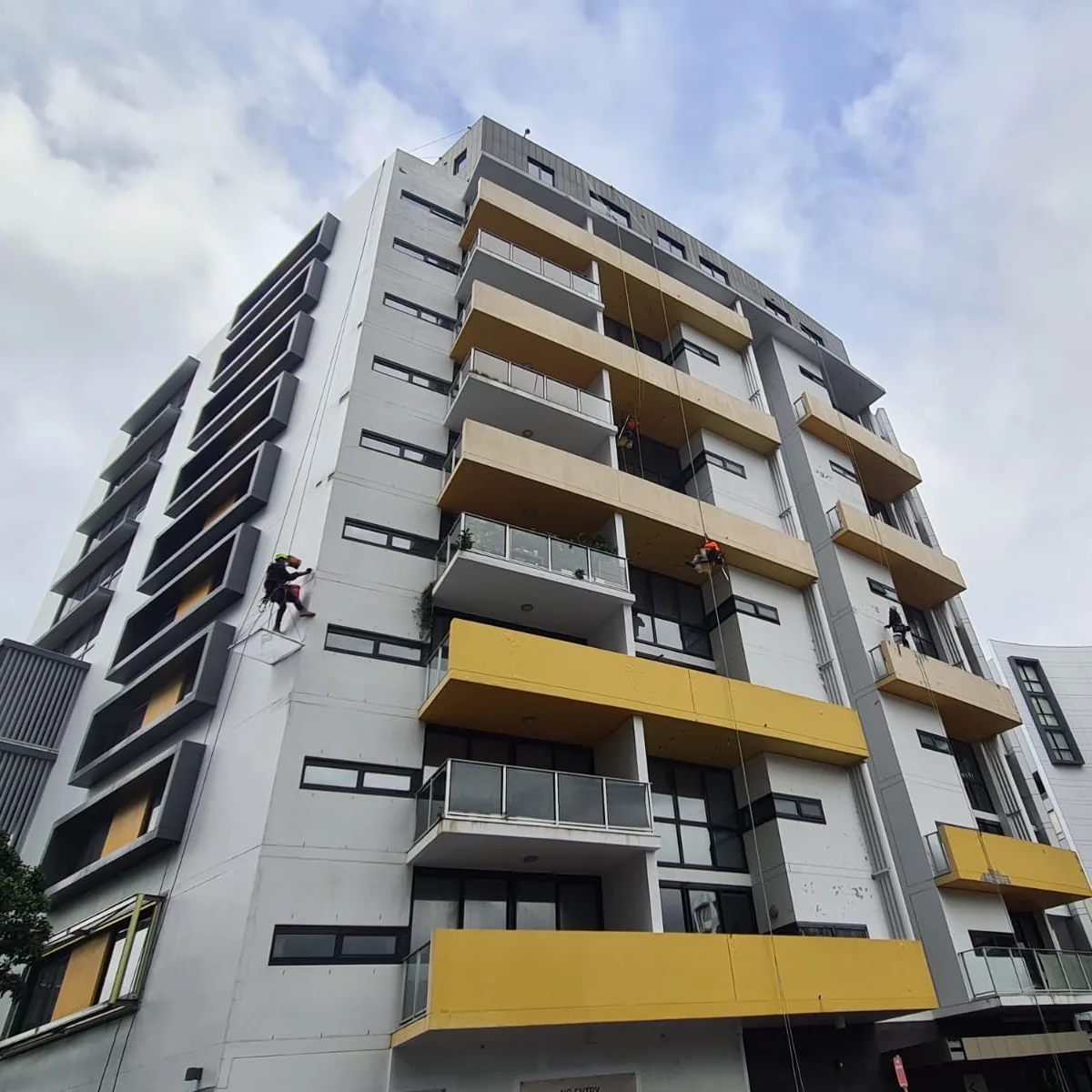 Rope access technicians complete concrete repairs to the side of a multi level building before painting, Sydney
