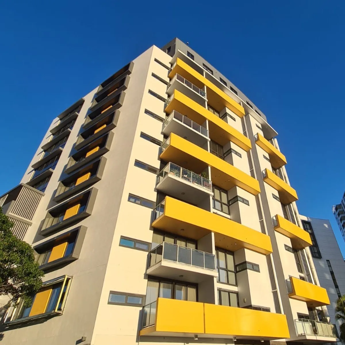 Apartment tower facade repainted cream with yellow balconies after rope-access painting, Sydney