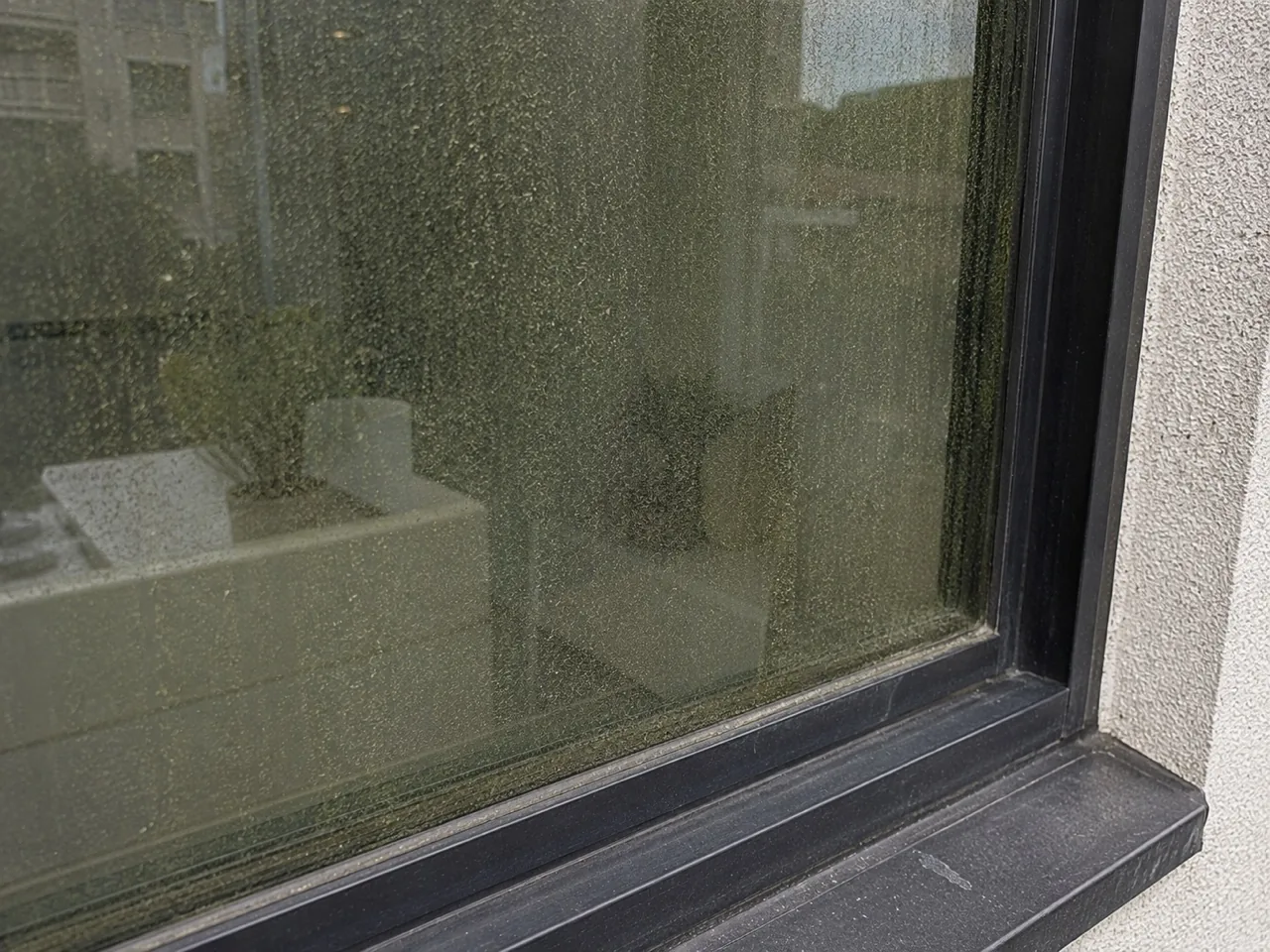 Exterior window glass and frame filmed with dark organic soiling and mineral streaking