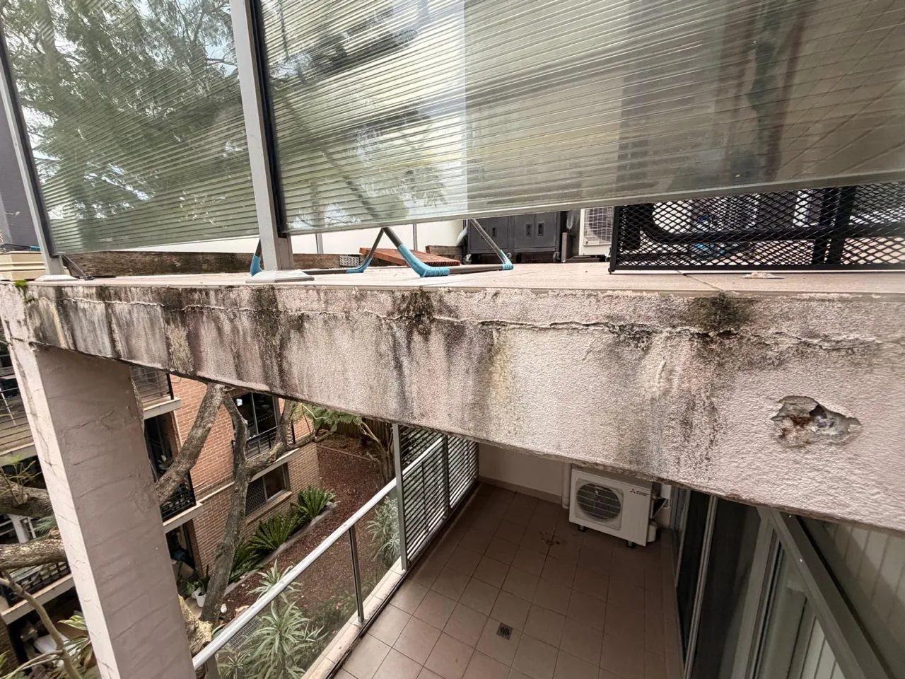 Underside of a balcony slab with heavy staining, biological growth and edge spalling
