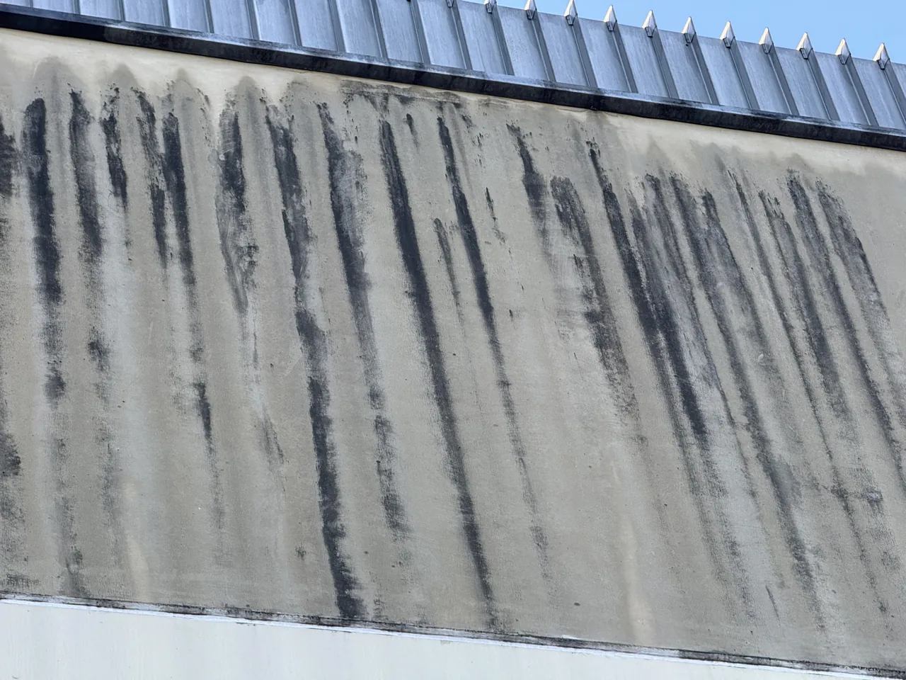 Heavy vertical dirt streaking down a rendered wall below a metal roof edge