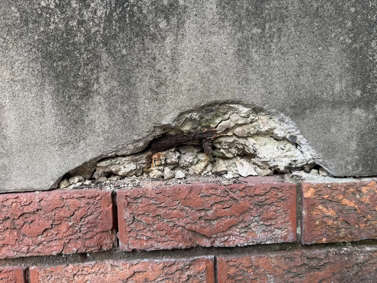 Render blown away above brickwork exposing corroded steel and crumbling substrate