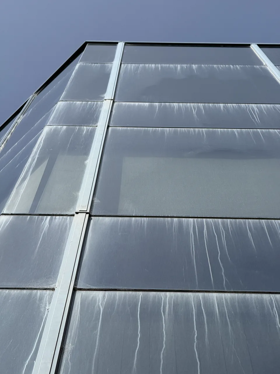 Upward view of a glazed facade with white mineral leaching streaks down each panel