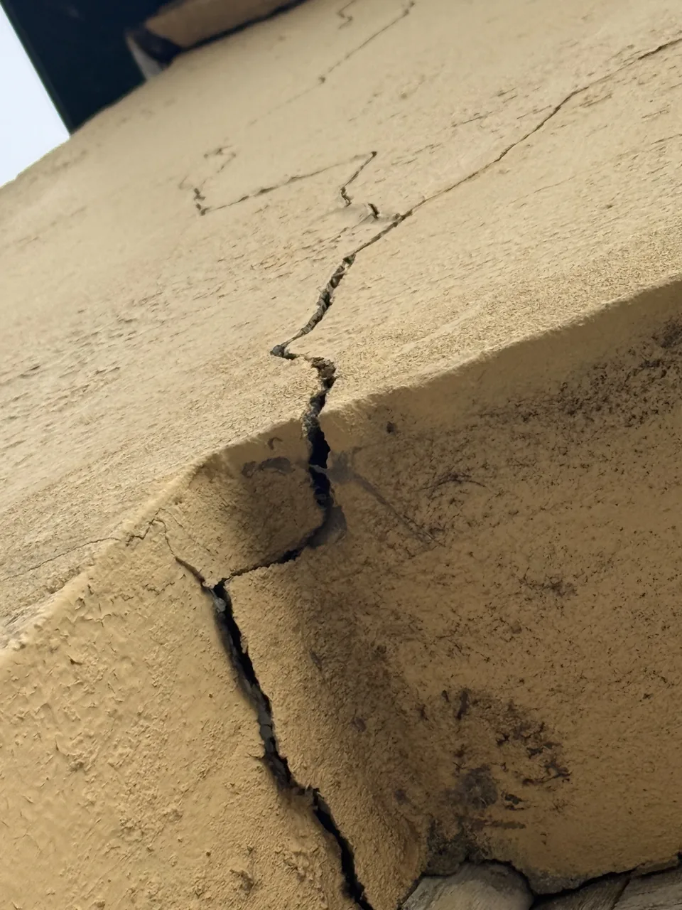 Deep stepped crack running through render at the corner of a structural column