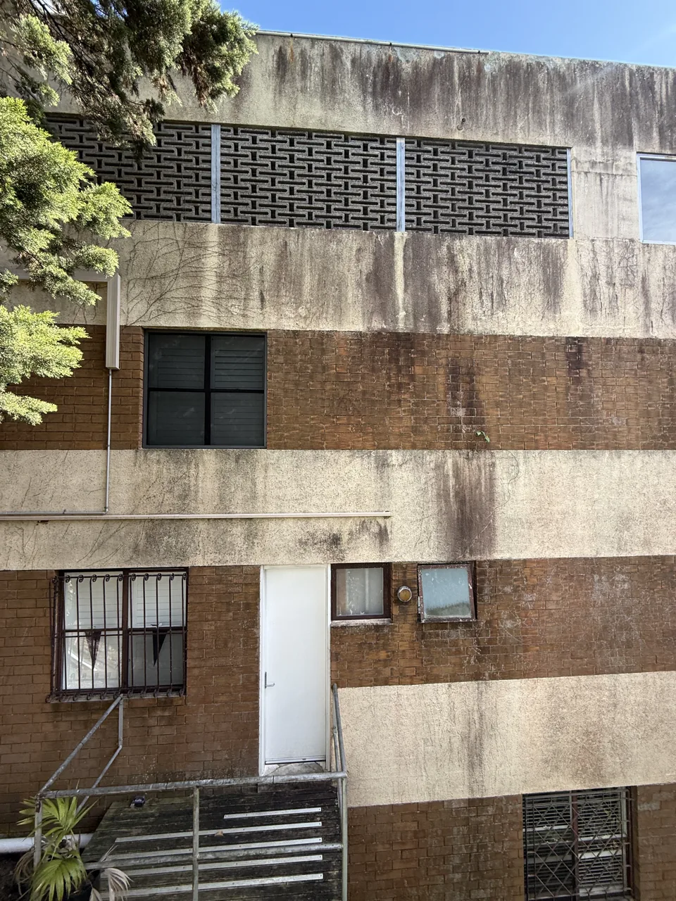Brick and render facade with heavy banded dirt staining and biological growth across multiple levels