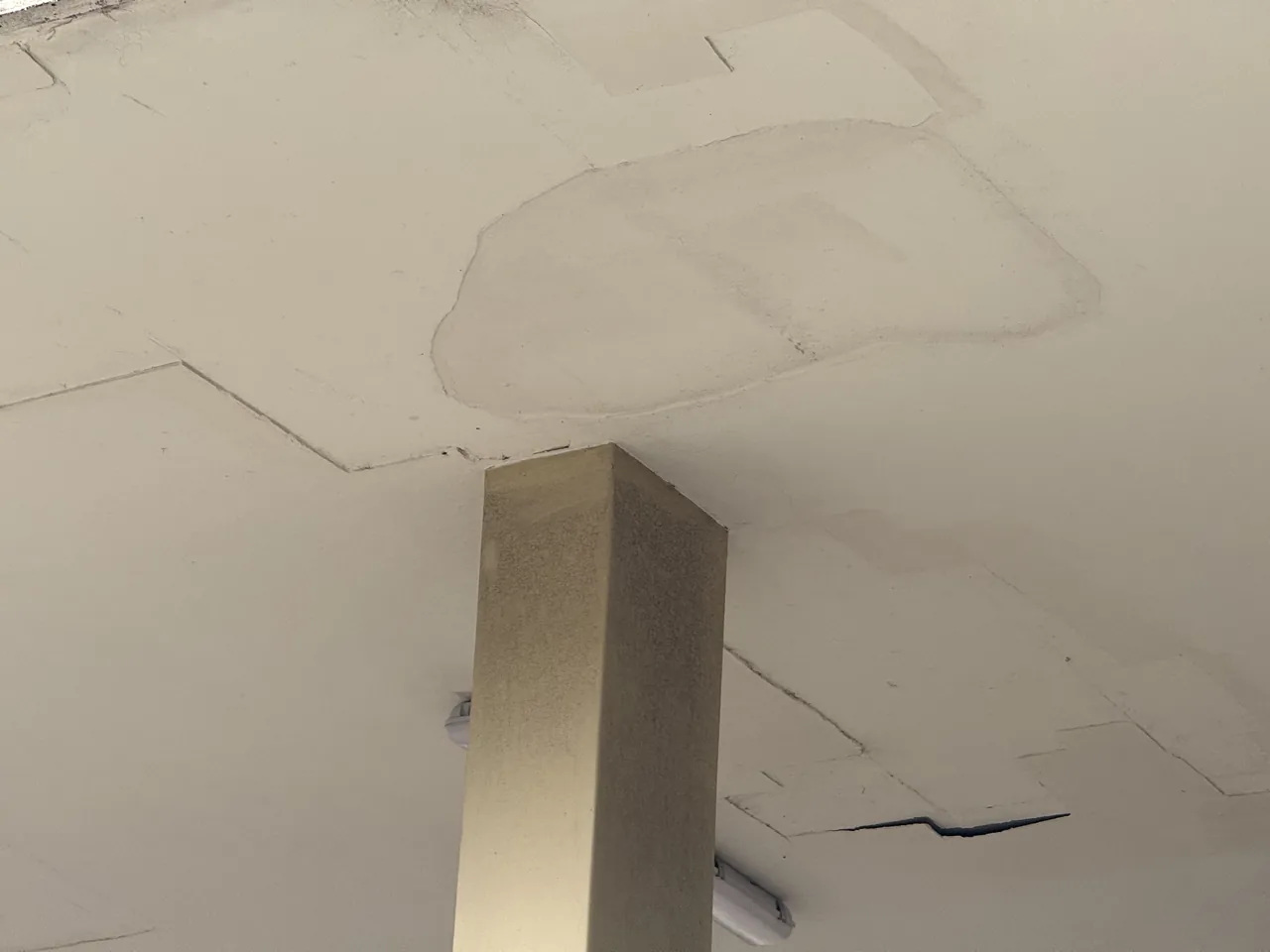 Ceiling with cracks, water stains, and peeling paint near a square column and light fixture.