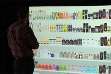 Shopper evaluating products at an illuminated retail simulation shelf wall in L&E Research's Cincinnati sensory evaluation research facility
