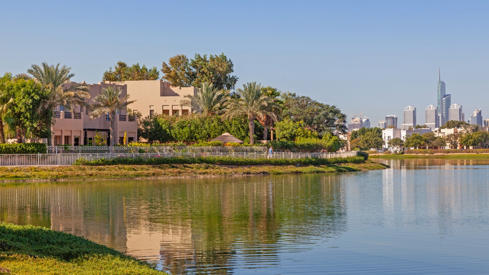Waterfront residential area with palm trees, greenery, and city skyline in the background under clear sky.