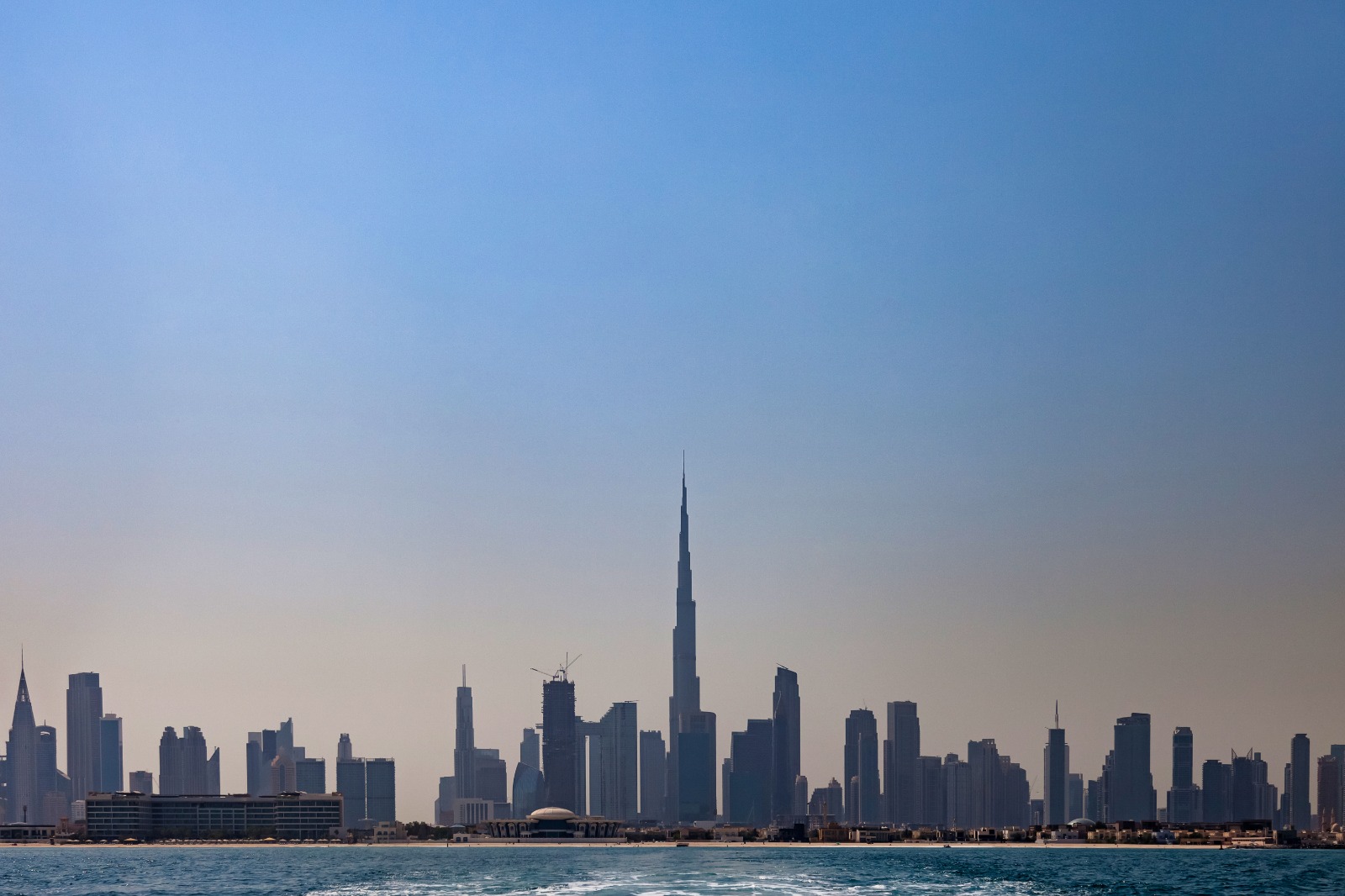 Skyline of Dubai with Burj Khalifa towering above other skyscrapers by the water.