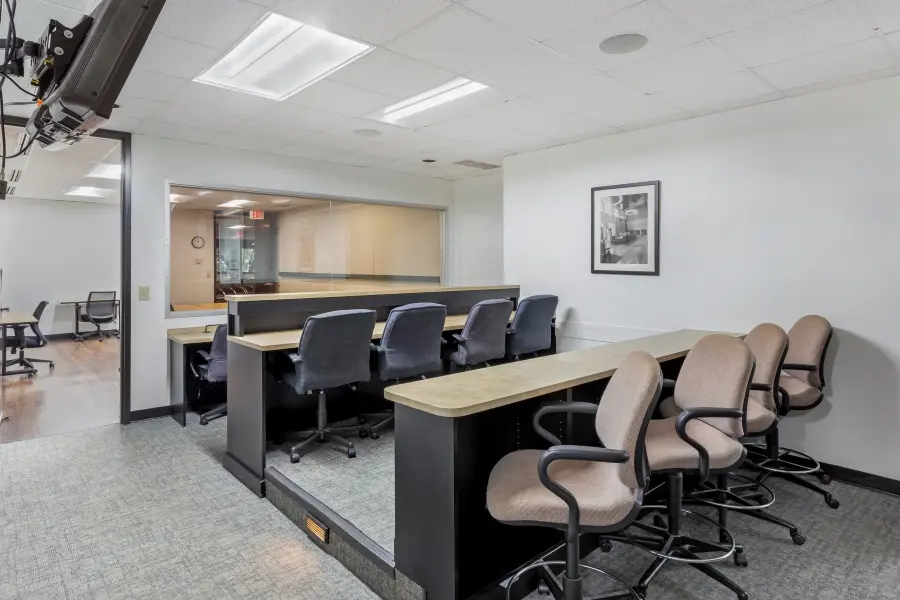 Dedicated client observation room behind a large one-way mirror overlooking the Biltmore suite research panel at L&E Research Raleigh.