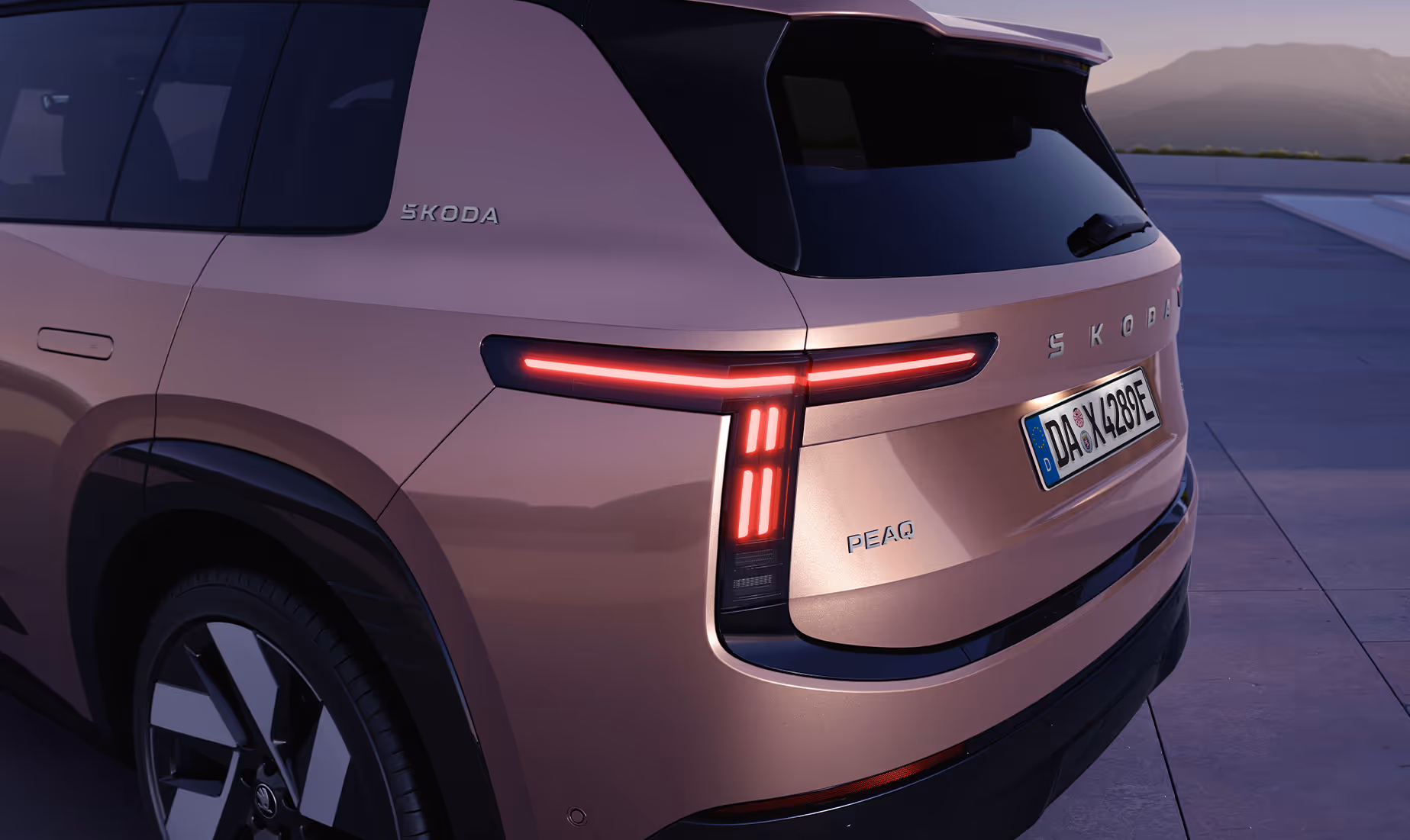 Detailaufnahme der linken Heckpartie des Škoda Peaq in der Lackierung Rosewood-Beige Metallic. Im Fokus der Ansicht steht die moderne LED-Rückleuchte mit ihrer markanten, mehrteiligen Leuchtgrafik, die sich bis in den Kotflügel zieht. Abgerundet wird das Heckdesign durch den zentralen Škoda Schriftzug auf der Heckklappe, den darunterliegenden Modellnamen "PEAQ" sowie einen weiteren dezenten Marken-Schriftzug an der breiten D-Säule.