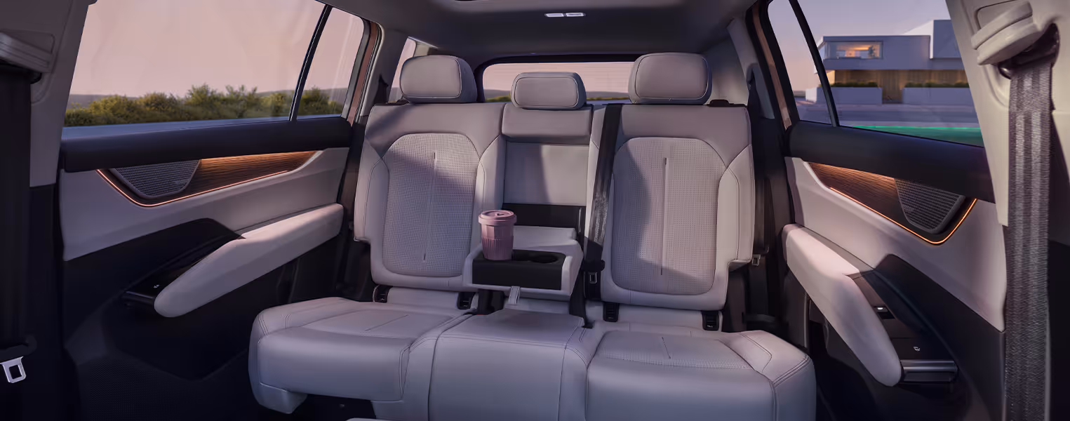 Blick in den Fond des Škoda Peaq auf die geräumige Rücksitzbank, die passend zum restlichen Interieur in hellen Keramikfarben gehalten ist. Die mittlere Sitzlehne ist als bequeme Armlehne heruntergeklappt, in deren integriertem Getränkehalter ein Becher steht.