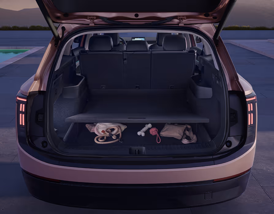 Blick in den geöffneten Kofferraum des Škoda Peaq in der Lackierung Rosewood-Beige Metallic. Der variable Ladeboden bildet hier eine obere Ebene und gibt ein praktisches Unterfach frei, in dem verschiedene Hundeutensilien wie Leine und Spielzeug ordentlich verstaut sind. Im Hintergrund ist die aufgestellte Rücksitzbank des dunklen Interieurs zu erkennen.