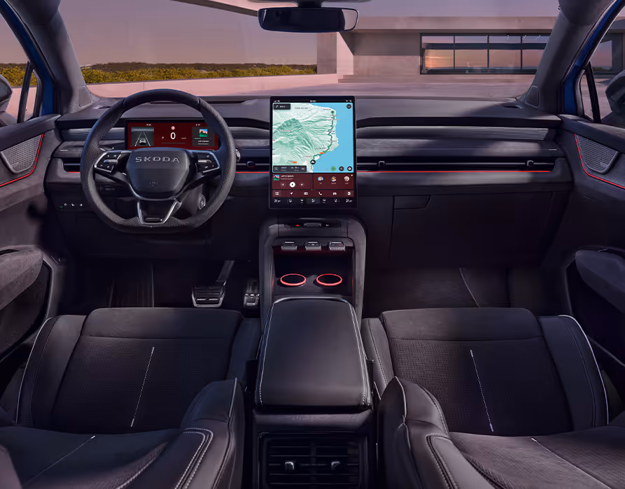 Symmetrischer Blick aus dem Fond in das abgedunkelte Cockpit des Škoda Peaq mit der sportlichen Innenausstattung "Design Selection Sportline". Das Interieur wird von schwarzen Sitzen mit hellen Kontrastnähten, einem unten abgeflachten Multifunktionslenkrad und dem großen, zentralen Infotainment-Display geprägt. Eine markante rote Ambientebeleuchtung entlang der Armaturentafel und in der Mittelkonsole unterstreicht den dynamischen Charakter des Fahrzeugs.