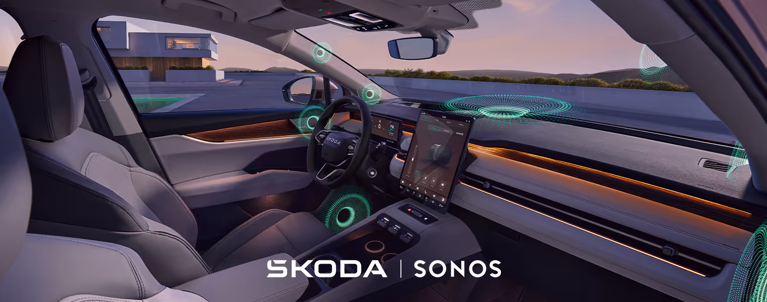 Blick von der Beifahrerseite in das aufgeräumte, keramikfarbene Cockpit des Škoda Peaq im sanften Abendlicht. Über den gesamten Innenraum an Türen, Armaturentafel und Fußraum verteilt, visualisieren grafisch eingeblendete, grüne Schallwellen die Positionen der verschiedenen Lautsprecher des optionalen Sonos Soundsystems. 