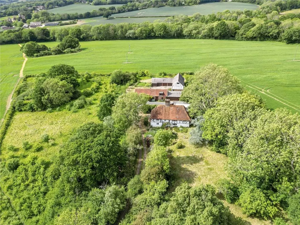 Aerial view of a countryside house with red roof surrounded by trees and green fields.