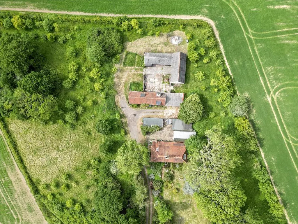 Aerial view of a rural property with several buildings surrounded by green fields and trees.