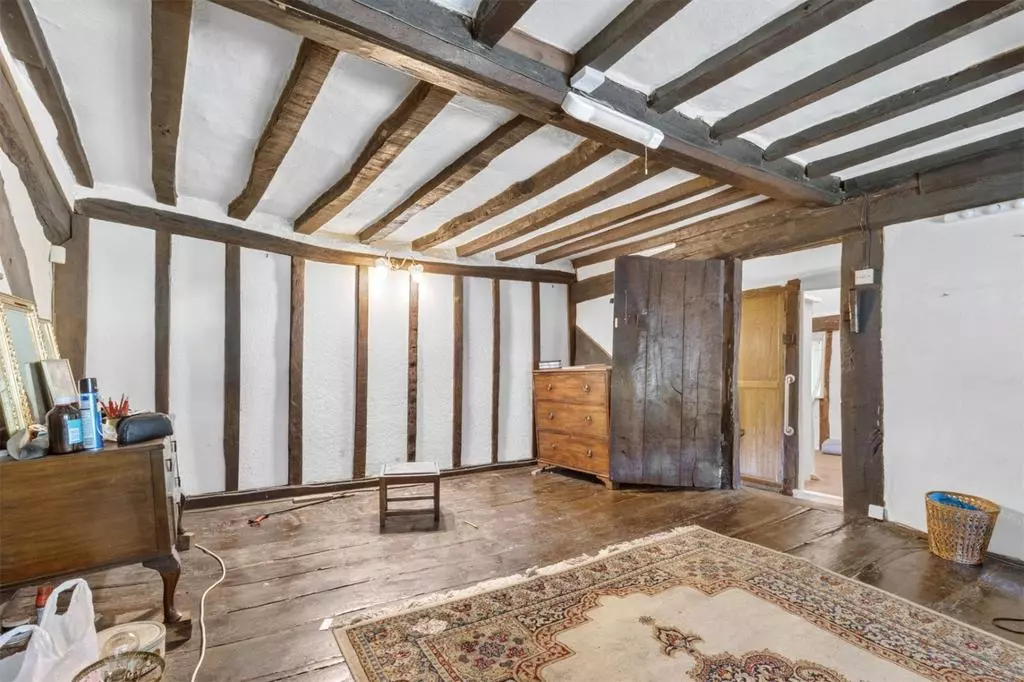 Rustic room with exposed wooden beams, a patterned rug, wooden dresser, open door, and stool on wooden floor.