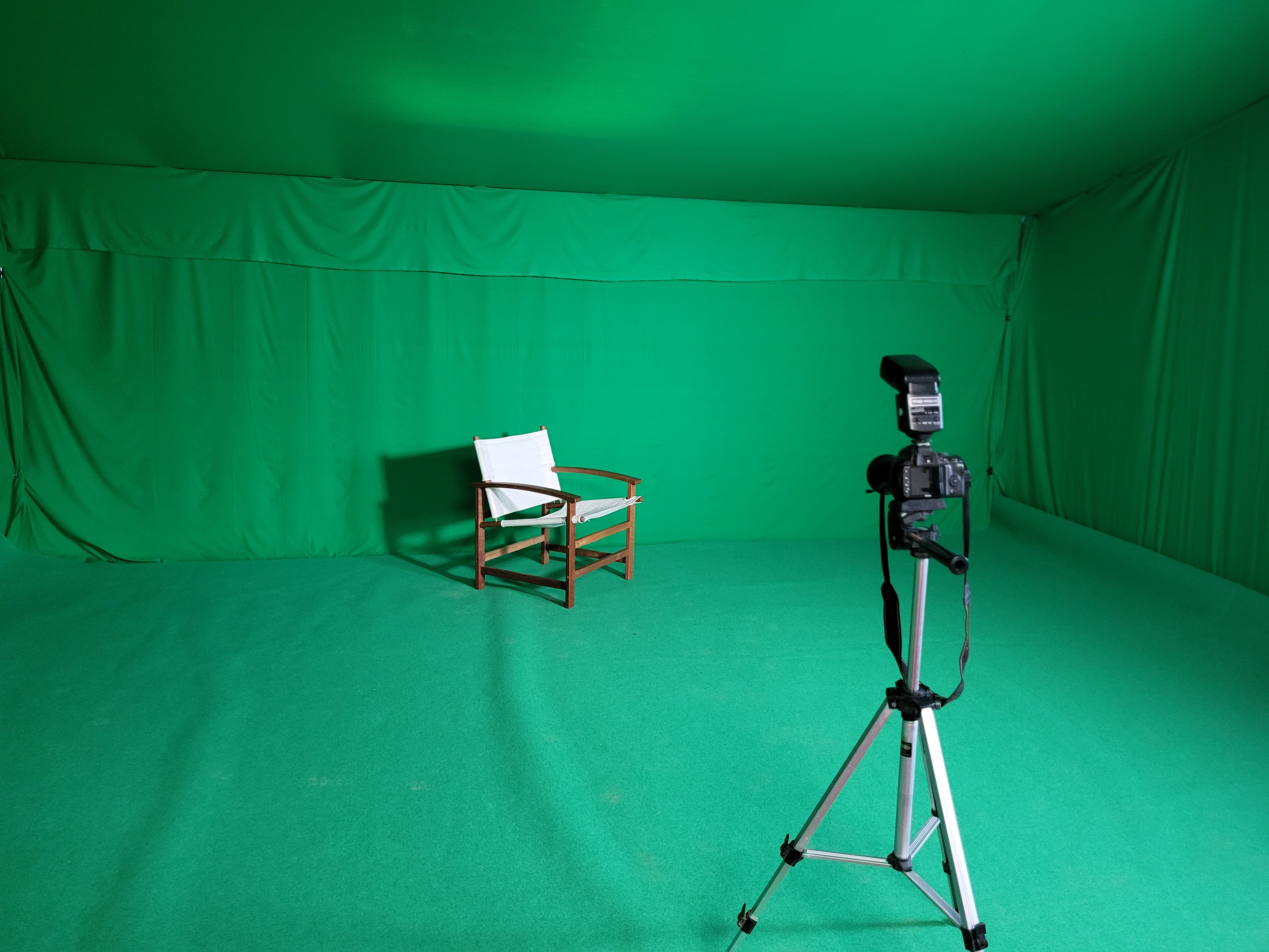 Wooden chair with white cloth in a green screen studio with camera on tripod in front.